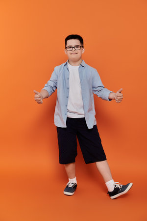 Young boy with Down syndrome smiles, arms outstretched in front of orange backdrop.