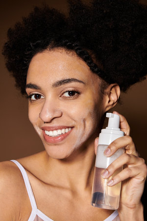 A young African American woman smiles while holding a bottle of facial cleanser.の写真素材