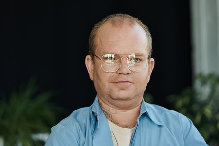 A man with inclusivity with glasses looks directly at the camera with a focused expression.