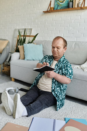 A man with inclusivity sits on the floor, writing in a notebook, in a casual, relaxed setting.の写真素材
