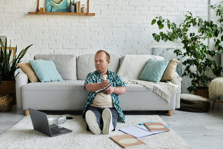A man with inclusivity sits on the floor of a living room, focused on writing in a notebook.