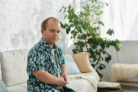 A man with inclusivity sits on a couch in a living room, looking thoughtfully ahead.の写真素材
