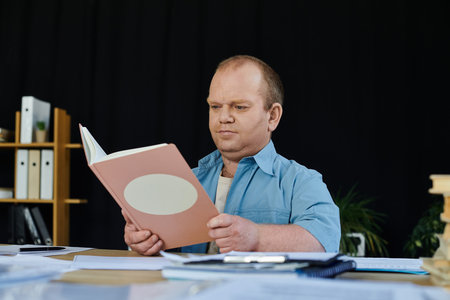 A man with inclusivity sits at a desk reading a book.