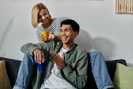 A young interracial couple relaxes on a couch in a modern apartment, enjoying a cup of coffee and each others company.の写真素材