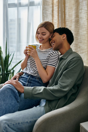 A young, multicultural couple shares a cup of coffee and a loving moment in their modern apartment.の写真素材