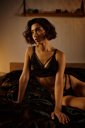 A young woman in black lingerie lies on a bed, her gaze soft and seductive.の写真素材