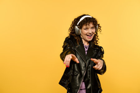 A young woman with curly hair, wearing a black leather jacket, poses confidently with a bright smile, against a vibrant yellow backdrop.の写真素材