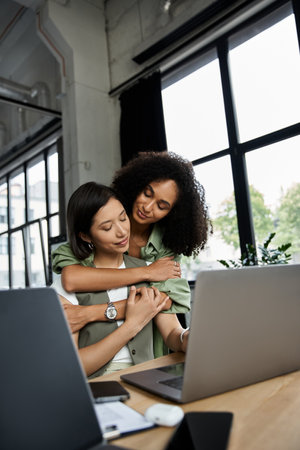 Two women, a lesbian couple, embrace in a modern office setting.の写真素材