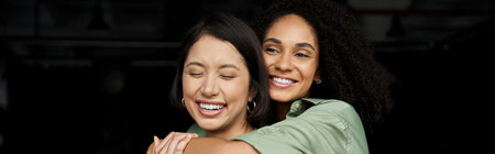 Two women hug each other in an office setting, both smiling and laughing.