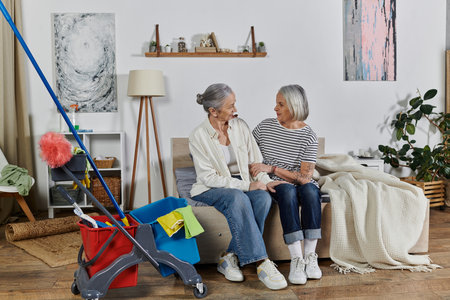 A mature lesbian couple relaxes on a couch after cleaning their modern apartmentの写真素材