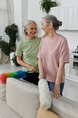 A mature lesbian couple smiles as they clean their modern apartment together.