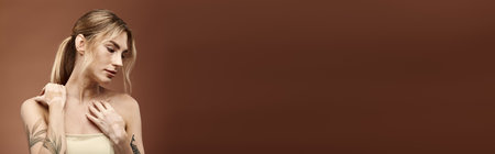 A young woman with vitiligo and a tattoo poses with her shoulders bare against a beige background.の写真素材