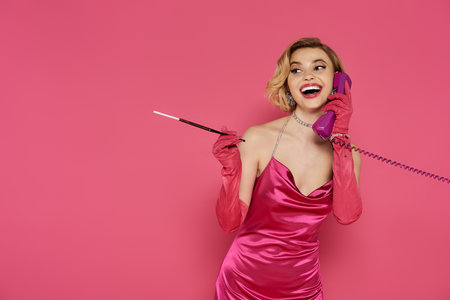 A stylish woman in a pink dress conversing on a phone.