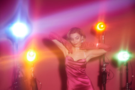 A woman in a vibrant pink dress dances under colorful lights.