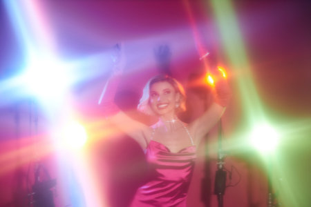 A woman in a pink dress dances under colorful lights.