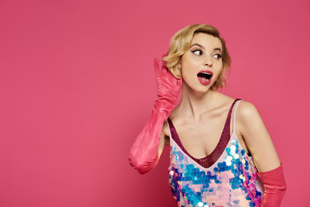 A woman in a sequined top and pink gloves leans in to listen, her lips parted in anticipation.の写真素材