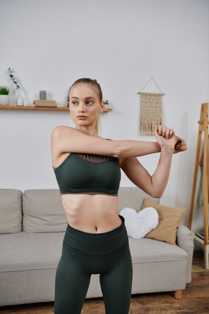 A young woman in athletic wear stretches her arms in her living room.