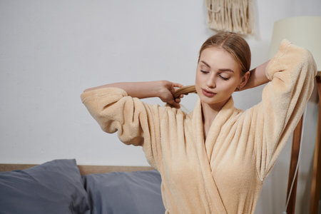 A young woman in a plush robe stands in her bedroom, a moment of quiet peace before the day begins.の写真素材