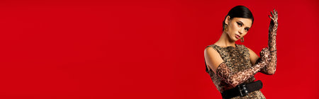 A young woman poses in a leopard print dress and gloves against a red background.の写真素材