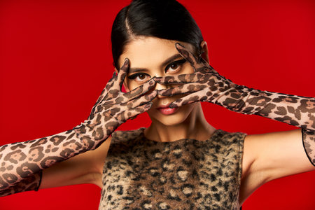 Woman in leopard print gloves & dress poses mischievously against red backdrop.の写真素材