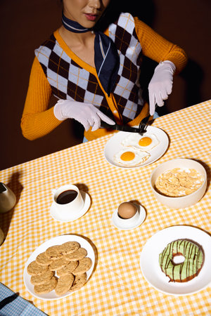 A fashionable woman sits with eggs, coffee, and treats.の写真素材