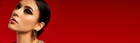 A young woman with dark hair and bold makeup poses against a red backdrop.の写真素材