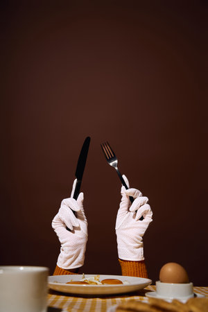 A pair of gloved hands holding a knife and fork, poised over a plate of food.