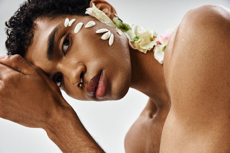 A young, muscular African American man with flowers on his face and body poses against a grey backdrop, showcasing beauty and diversity.の写真素材