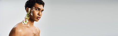A young, muscular African American man poses against a grey backdrop with flowers adorning his face and body.の写真素材