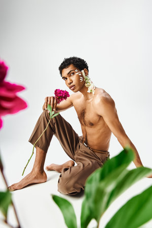 A young, muscular African American man poses with flowers on his body and face against a grey background, celebrating beauty and diversity.の写真素材