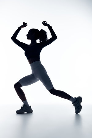 A young Black woman in athletic wear performs a dynamic lunge against a stark white background.の写真素材