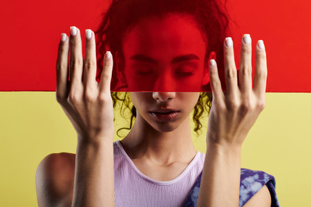 A young African American woman poses in a studio setting, holding a red panel in front of her face.の写真素材