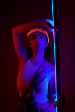A young African American woman poses in a studio lit by neon lights, showcasing a sporty and...