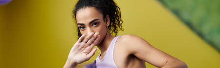 A young woman with curly hair poses in a studio with bright neon lights.
