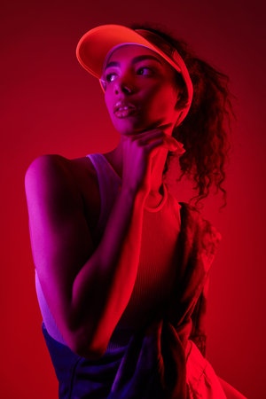 A young woman with curly hair poses in a studio with vibrant neon lighting.の写真素材