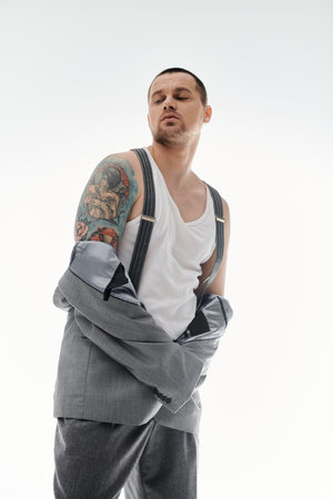 A stylish man in a white tank top and grey suit stands against a white background.