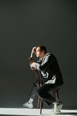 A man in a stylish gray suit sits thoughtfully on a chair, lost in thought.