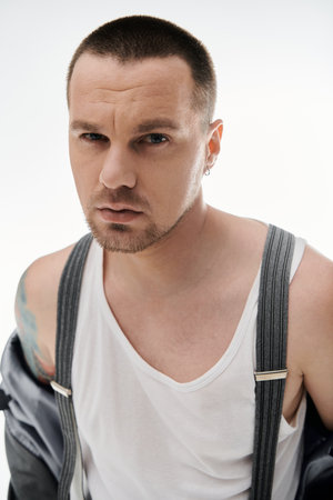 A man with a stylishly short haircut and a white tank top stares intensely at the camera.