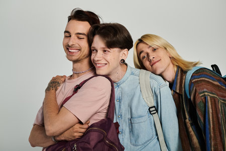 Three young students, part of the queer community, stand together in casual attire on a grey...
