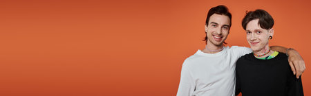 Two young friends in vibrant attire pose together against an orange backdrop.の写真素材