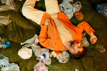 A man lies on the grass, surrounded by plastic waste.の写真素材