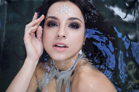 A young woman with dark hair and a shimmering jewel on her forehead floats in an aquarium.の写真素材