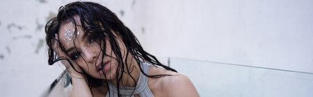 A young woman with wet brunette hair sits in an aquarium, gazing sadly into the distance.