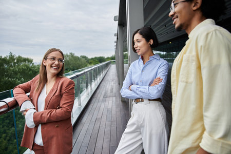 Three colleagues enjoy a casual conversation on a rooftop terrace at a modern office.の写真素材
