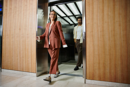 A woman with a prosthetic leg exits an elevator and smiles warmly near colleague who is stepping...