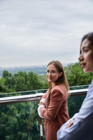 Two diverse colleagues stand on a rooftop terrace, chatting and enjoying the view.の写真素材