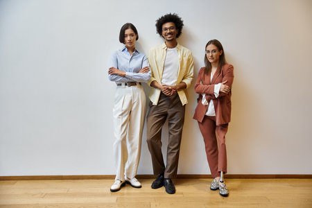 Three colleagues stand in a modern office, smiling and looking confident.の写真素材