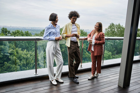 Three colleagues chat and laugh on a modern rooftop terrace.の写真素材