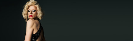 A drag queen with dramatic makeup and a blonde wig poses in a long black dress against a dark gray background.の写真素材