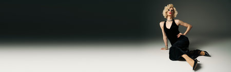 A drag queen with a blonde wig and dramatic makeup poses in a long black dress against a grey backdrop.の写真素材